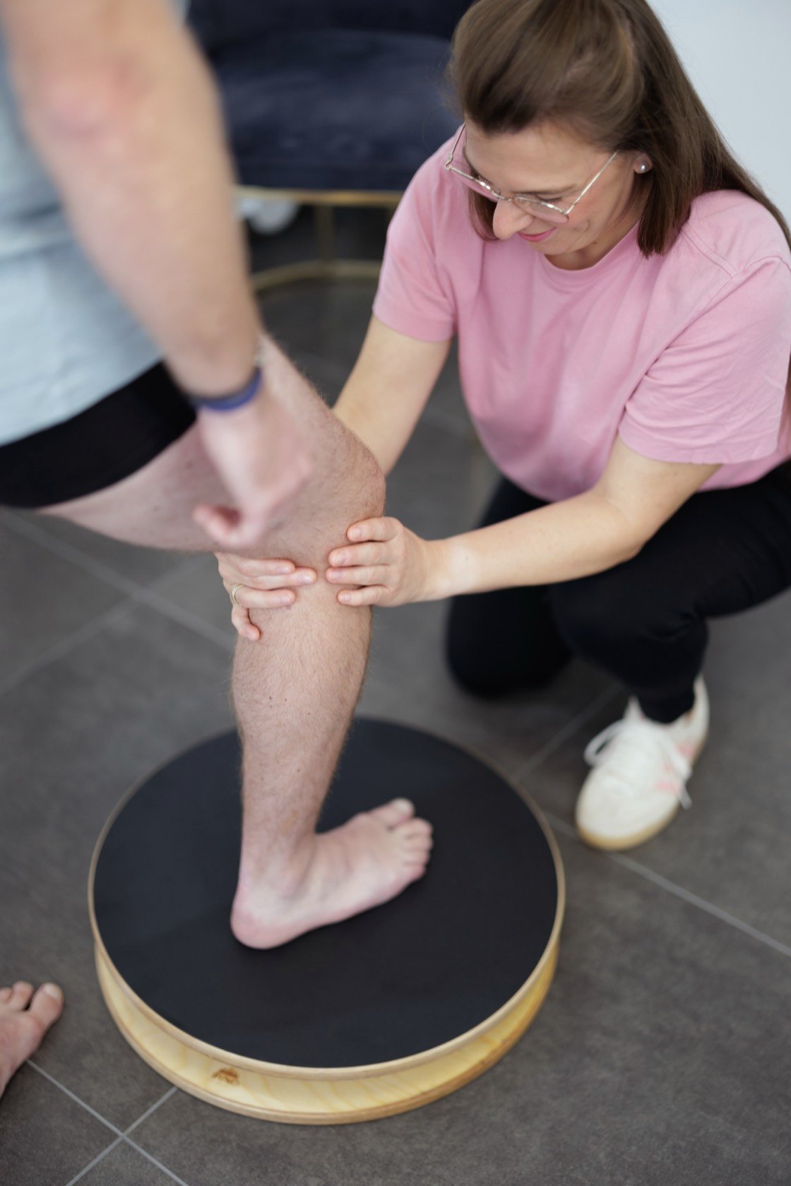Physiotherapeutin sichert das Knie eines Patienten bei einer Übung auf dem Balance-Kreisel