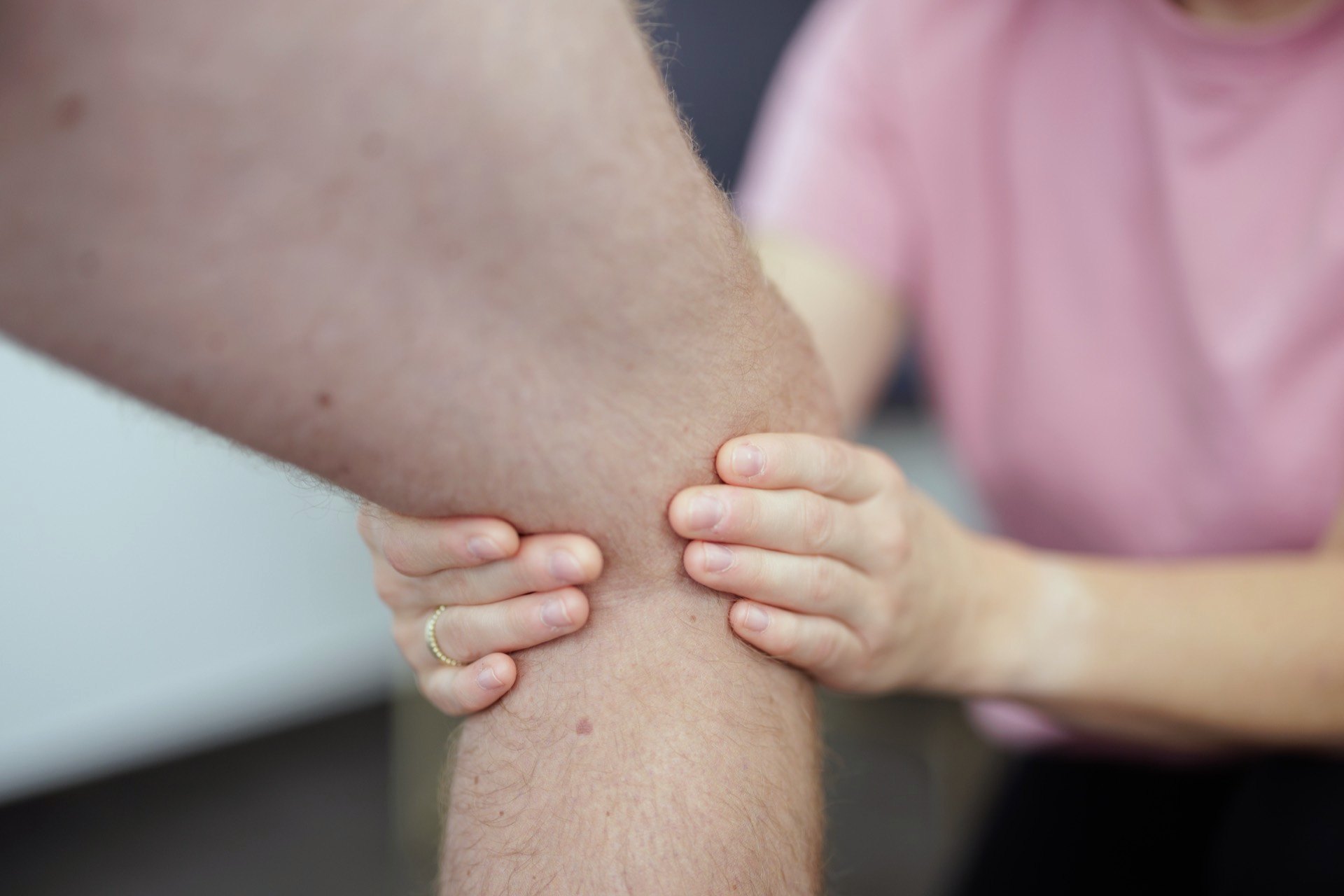 Physiotherapeutin untersucht mit beiden Händen das Knie eines Patienten