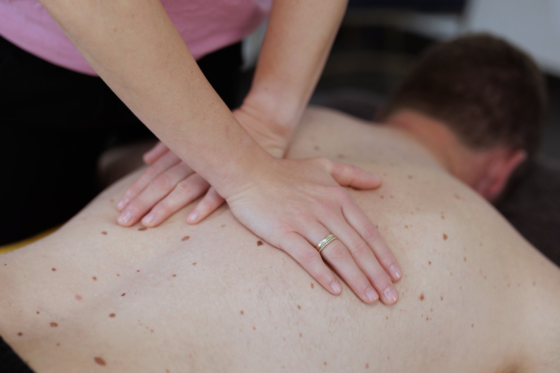 Physiotherapeutin behandelt mit beiden Händen den Rücken eines Patienten