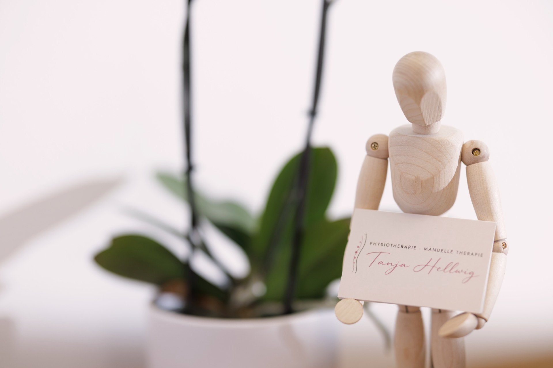 Holzfigur mit der Visitenkarte der Praxis vor einer Orchidee